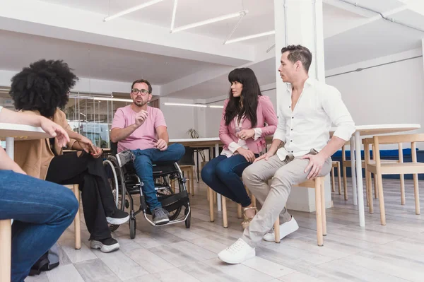 Caucasian Hispanic Latino adult man, with beard, glasses and in a wheelchair meeting and talking with other people of different genders and ethnicities, in meeting making a business plan.