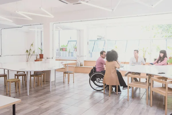 Mixed Hispanic Latino business people of different genders and ethnicities, gathered in a large green office with natural light with wooden tables and chairs and plants.