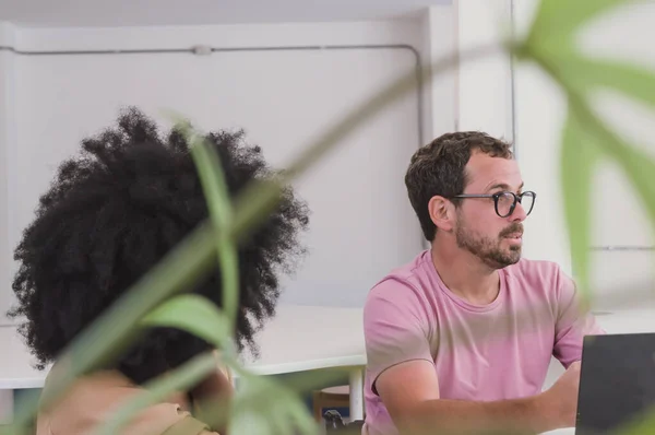 Hispanic Latino bearded man with glasses speaking and explaining meeting with his computer, with a blurred plant frame in front of him, in an ecological office in a coworking.
