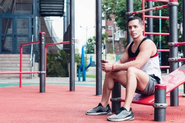 Genç, atletik, beyaz tenli Latin atlet, bir spor salonunda, dışarıda oturuyor, konuşuyor..