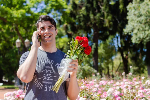 Latynoski Biały Młody Człowiek Trzymając Czerwone Kwiaty Szczęśliwy Uśmiech Parku — Zdjęcie stockowe