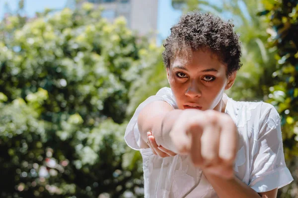 portrait of strong young brunette hispanic latin woman in from view, with short hair, punching with clenched fist and looking at the camera, female inclusion and lifestyle concept.