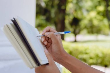 Kadın ellerinin bir defter tutarken ve dışarıda bir parkta kalemle notlar alırken, fotokopi alanı ile resim çekilirken..