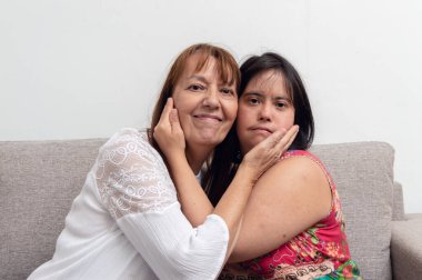 Oturma odasındaki kanepede oturup kameraya bakarken birbirlerinin yanaklarına dokunan Latin Arjantinli anne ve kızının portresi..