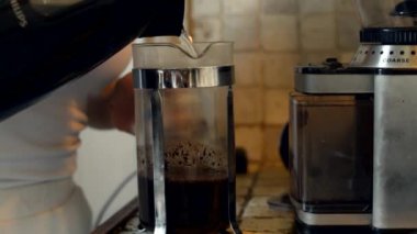 Genç, beyaz bir kadın manuel Fransız kahve makinesine sıcak su dökerek kahvaltıya kahve hazırlıyor..