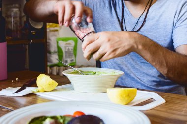 Arjantinli yetişkin adam mutfağında yemek pişiriyor beyaz kaseye tuz koyup ahşap masaya guacamole hazırlıyor..