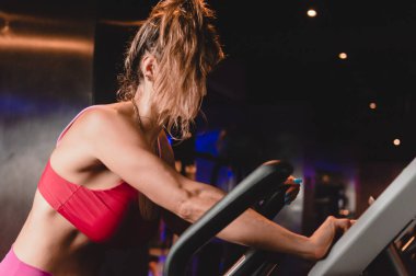 Taraftan bakıldığında, beyaz tenli güzel bir kadın spor salonunda eliptik antrenörde sağlıklı yaşam için kardiyo eğitimi alıyor..