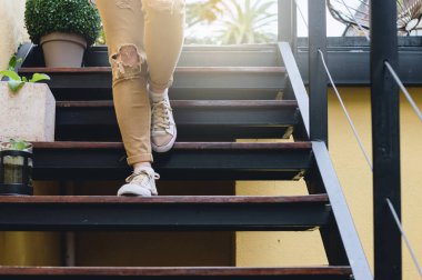 Hardal renkli pantolonu olan genç bir kadının ayaklarındaki ve bacaklarındaki ayrıntı merdivenlerden aşağıya iniyor..