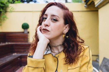 Kafkasyalı genç beyaz kadın sakince oturur, çenesini eline dayar kameraya bakar, düşünür, sarı günlük kıyafetler giyer, yaşam tarzı kavramı oluşturur..