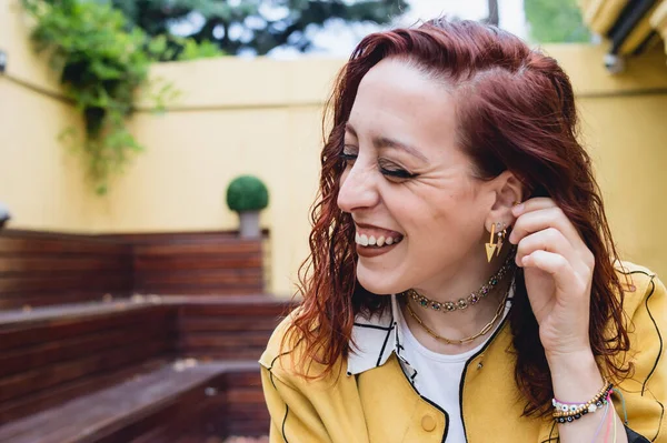 Kafkasyalı, genç, kızıl saçlı, gözleri kapalı ve günlük kıyafetleriyle gülümseyen bir kadın. Küpe takıyor, evin bahçesinde oturuyor.