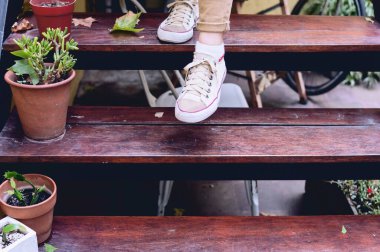 Yakın çekim ön manzara. Dışarıdaki ahşap merdivenlere ayak basıyor. Merdivenleri de bitkilerle süslüyor..