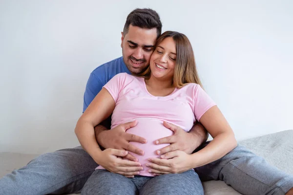 幸せな白人妊娠中の女性と彼女の夫はベッドの上に座っ笑顔とおなかの上に赤ちゃんに触れます 妊娠療法と運動ルーチンを行います — ストック写真