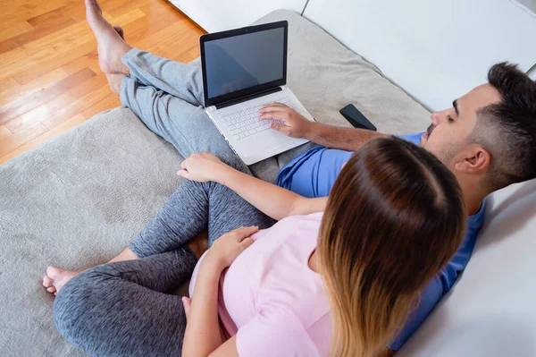 顶级后视镜怀孕的拉丁裔夫妇坐在床上 观看笔记本电脑屏幕 使用电脑 上网购物和观看系列节目 — 图库照片