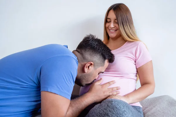 白人男性はベッドの上でベッドの上に座ってキスをしながら妊娠中の妻の腹に触れ — ストック写真