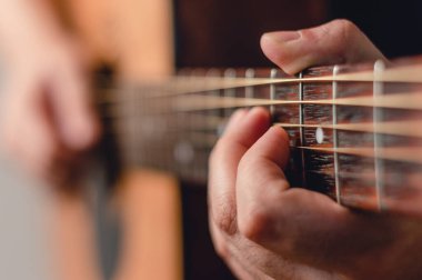 Kafkas erkek eli akustik gitar akoru yapıyor, fret ve parmaklara odaklanıyor, soldaki boşluğu kopyalıyor..