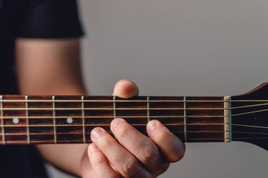 Erkek elinin akustik gitar ensesinde ön plan detayı, bulanık arka plan ve kopyalama alanı, el ve tellere odaklanma, çevrimiçi müzik kursları için kaynaklar.