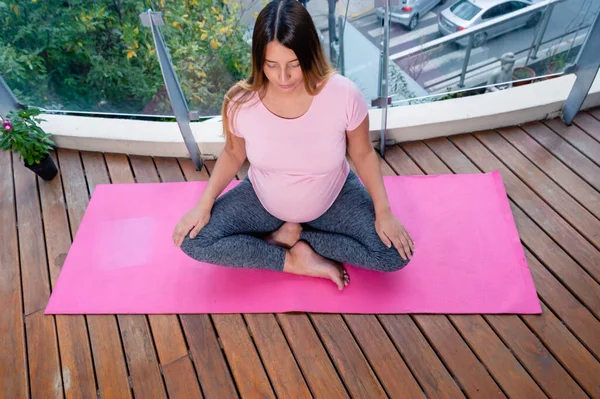 上角ビュー妊娠中の若い女性でピンクで目を閉じてマットの上に座っ蓮の位置瞑想 ヨガの概念 — ストック写真