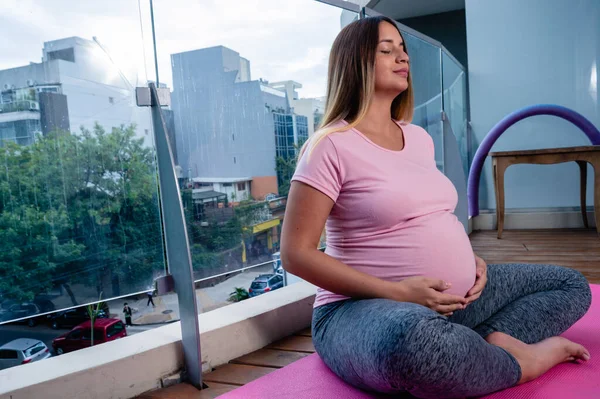 妊娠中の白人の若い女性がマットの上に座って瞑想しヨガを練習しています — ストック写真