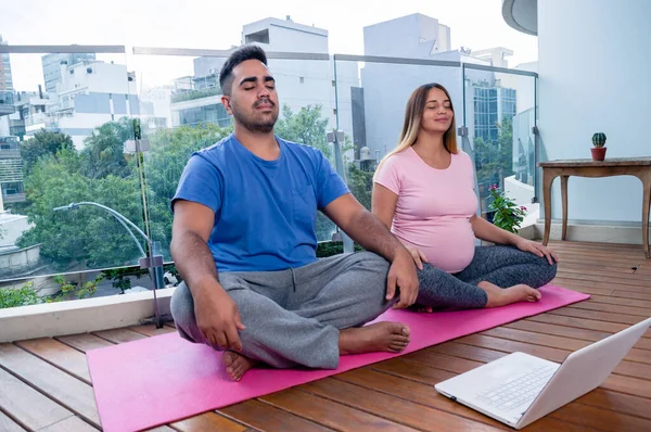 マットの上に座っている2人の男と妊婦ノートパソコンを持って家で目を閉じて蓮の位置で瞑想オンラインヨガクラスで — ストック写真