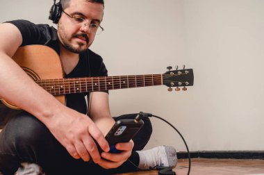 Kafkasyalı genç, gözlüklü ve kulaklıklı Latin bir adam. Müzik öğrencisi, yere oturmuş gitarını kontrol ediyor. Telefonu kontrol ediyor, mekanı kopyalıyor.