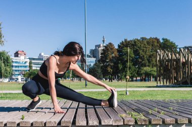 Yan görünüm genç Latin beyaz kadın ısınıyor ve bacak kasları geriniyor, sol bacak uzanıyor ellerle ayak parmaklarına dokunuyor, kopyalama alanı, fitness konsepti.