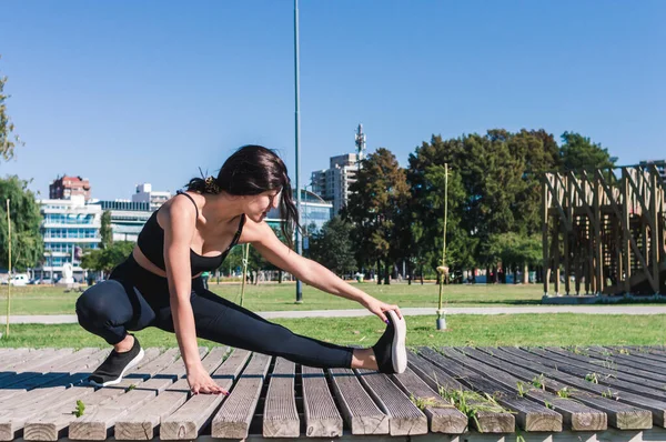 Yan görünüm genç Latin beyaz kadın ısınıyor ve bacak kasları geriniyor, sol bacak uzanıyor ellerle ayak parmaklarına dokunuyor, kopyalama alanı, fitness konsepti.