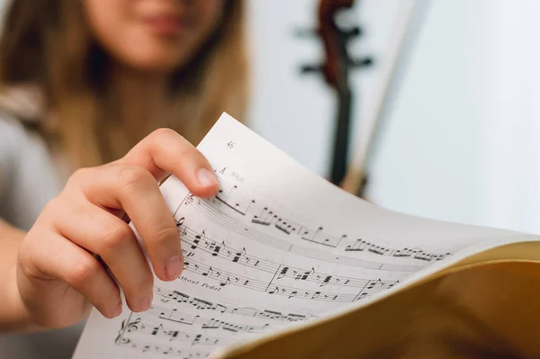 close up hand of a female violinist changing the page of the sheet music on the music stand. focus on hand. blurry woman in background with copy space.
