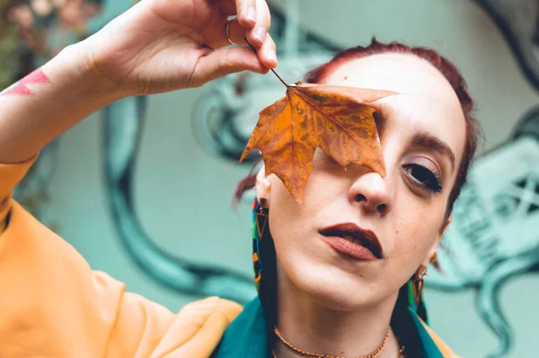 Arjantinli güzel bir genç kadın portresi, sarı, ciddi bir şekilde bir gözünü dışarıda bir sonbahar yaprağıyla kaplıyor, kameraya bakıyor..