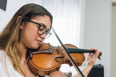 Güzel, beyaz tenli, Venezuelalı, gözlüklü, uzun saçlı bir kadın. Evdeki oturma odasında gözleri kapalı keman çalmaktan esinlenmişti.