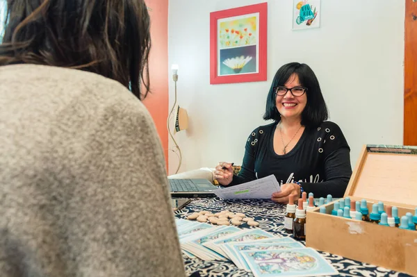 adult latin caucasian woman holistic doctor with glasses, sitting in her office smiling in the consultation attending a patient.