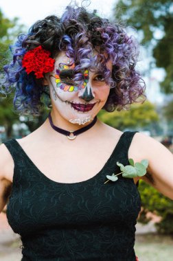 vertical portrait of beautiful young latin caucasian woman outdoors, looking at the camera, smiling and with La Calavera Catrina makeup.