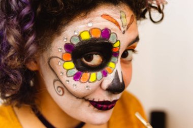 close-up portrait of young caucasian latin woman smiling and looking at the camera with La Calavera Catrina makeup in her room, preparing to celebrate the day of the dead.