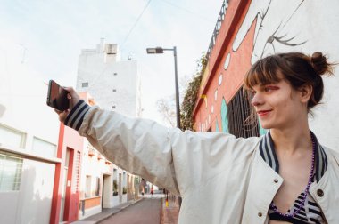 Evinin dışındaki Latin asıllı transseksüel kadının bir elinde telefonuyla selfie çekerken yan görüntüsü..