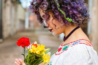 Mezarlıkta elinde bir buket çiçek olan ve yüzü La Calavera Catrina olarak boyanmış bir şekilde dua eden Latin bir kadının profil görüntüsü, Meksika geleneği, kopyalama alanı..
