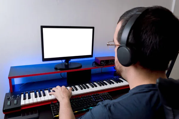 rear view of music producer with headphones, playing electric piano, sitting working remotely in his home music studio, copy space.