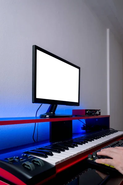 vertical side view of home music studio, with electric piano, monitor, audio interface and keyboard.