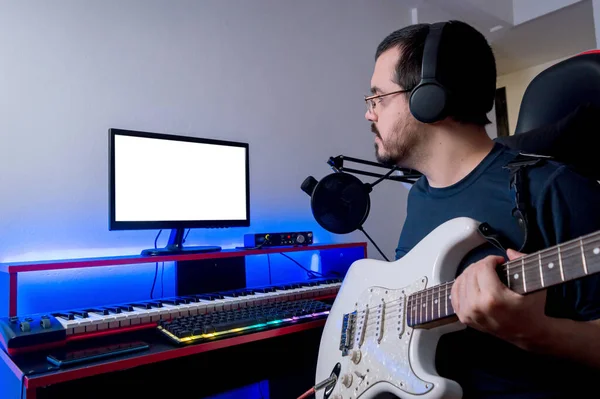 young latin caucasian man with a beard and glasses, sitting in his home music studio, checking the recording he made with his electric guitar, checking the audio tracks in the recording software.