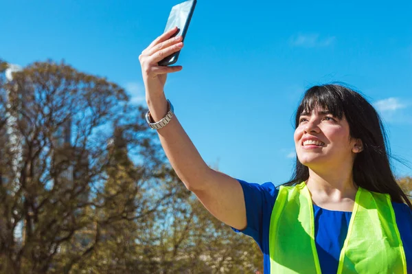 young latina venezuelan engineer woman at her job takes a selfie with her phone to send it to her boyfriend, technology concept, copy space.