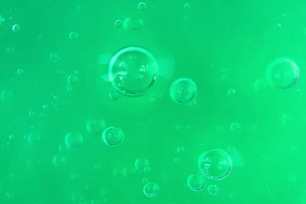 Texture of transparent green gel with air bubbles and waves on light monochrome background