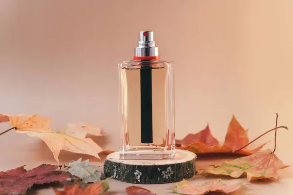 Flacon de parfum en verre transparent sur podium en bois avec des feuilles jaunes. Concept d'automne — Photo
