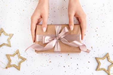 Doğal pembe manikürlü kadın elleri kraft kağıdında pembe kurdeleli bir hediye tutuyor. Xmas kompozisyonu. Düz yatıyordu