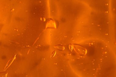 Turuncu zemin üzerinde hava kabarcıkları ve dalgaları olan şeffaf sarı jel dokusu