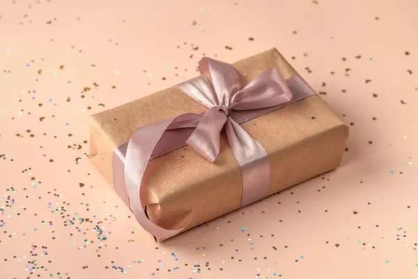 Verjaardag of Nieuwjaar aanwezig in kraftpapier met roze lint op zachte beige achtergrond met glitter. Kerstsamenstelling — Stockfoto