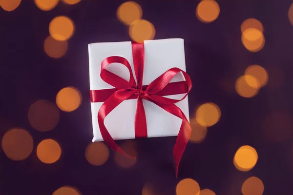 Caja de regalo envuelta en papel blanco con un lazo rojo rosado sobre fondo violeta festivo —  Fotos de Stock