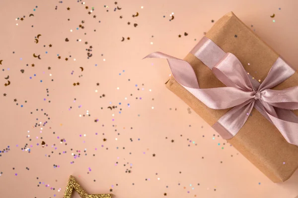 Verjaardag of Nieuwjaar aanwezig in kraftpapier met roze lint op zachte beige achtergrond met glitter. Kerstsamenstelling — Stockfoto