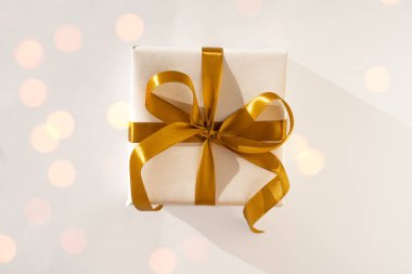 Beyaz kağıda sarılı bir hediye kutusu. Arka planda altın bir fiyonk var.