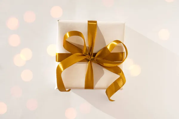 Beyaz kağıda sarılı bir hediye kutusu. Arka planda altın bir fiyonk var.