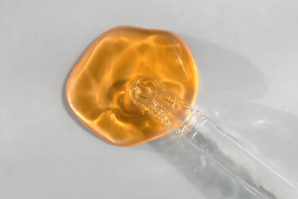 Pipeta s oranžovou tekutinou kyseliny hyaluronové na bílém pozadí. Koncept kosmetiky a zdravotní péče detailní záběr — Stock fotografie