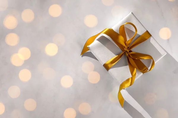 Beyaz kağıda sarılı bir hediye kutusu. Arka planda altın bir fiyonk var.