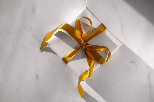 Caja de regalo envuelta en papel blanco con un lazo dorado sobre fondo claro festivo —  Fotos de Stock